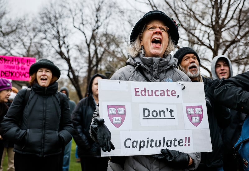 A protester holds a sign reading "Educate, Don't Capitulate!!" and Harvard University's  shields during a rally at Cambridge Common urging the Ivy League institution to resist President Trump's influence.